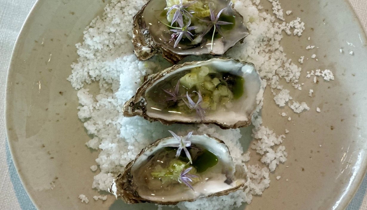 Tallerken med tre østers pyntet med grønn saus og lilla blomster