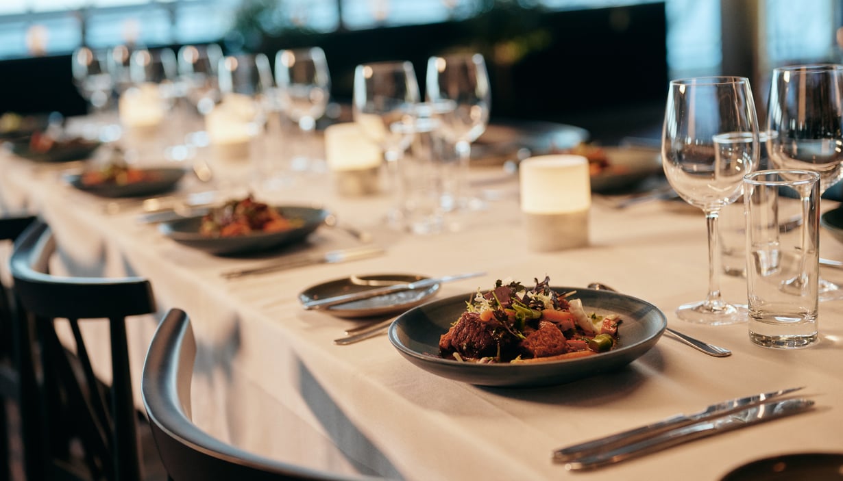 Elegant dekket spisebord med hvit duk, salat, bestikk, stearinlys og vinglass