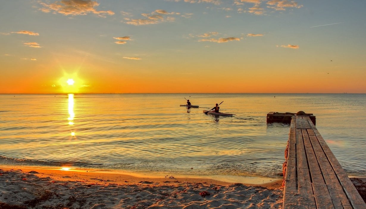 Fredelig strandscene ved solnedgang med to personer som padler kajakk.