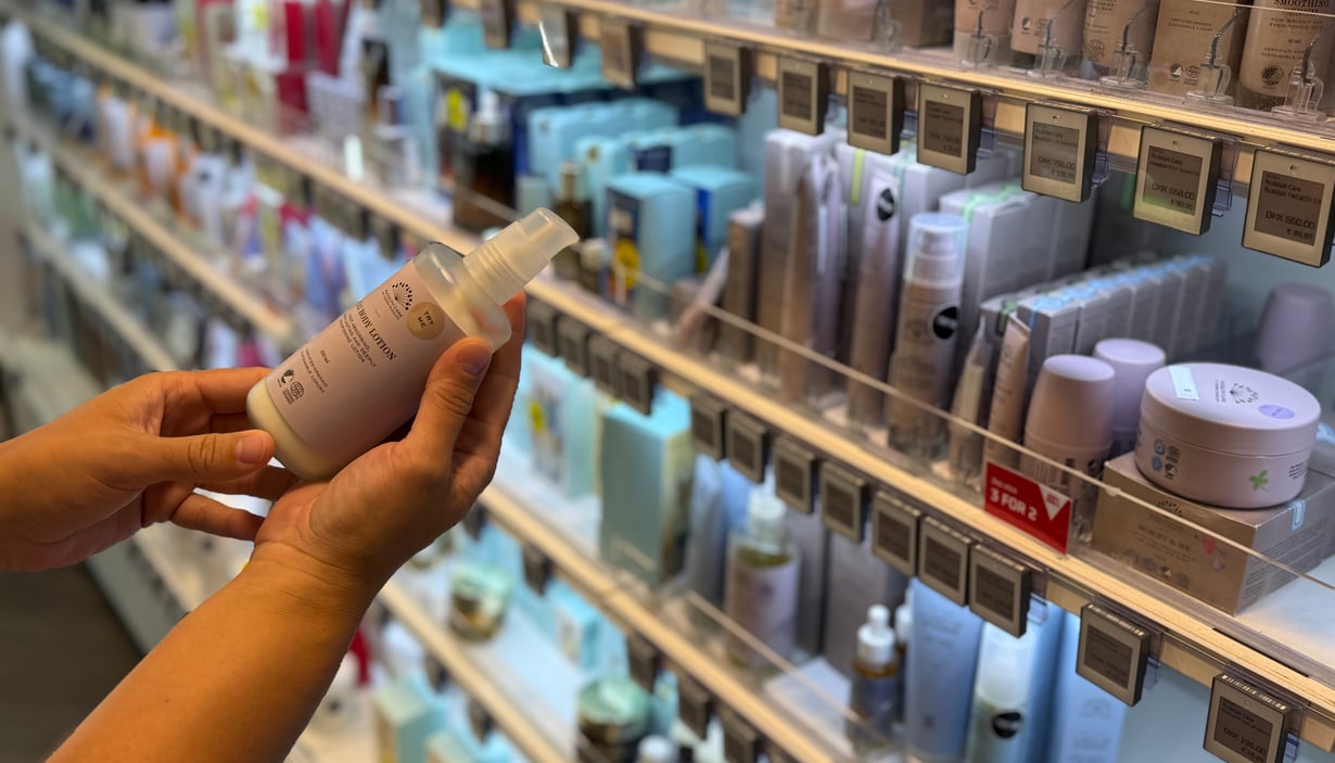 Person holder en hudpleieflaske i en butikkgang med skjønnhetsprodukter