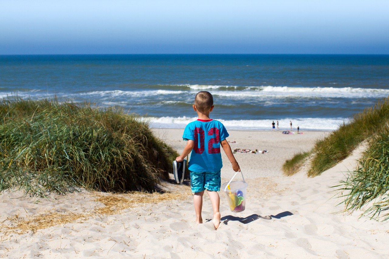 Barn som går ned en sandsti mot stranden.