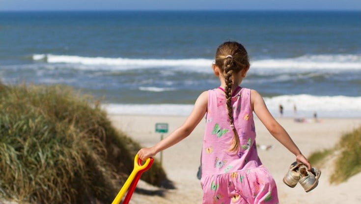Jente som går ned en sandsti mot stranden.