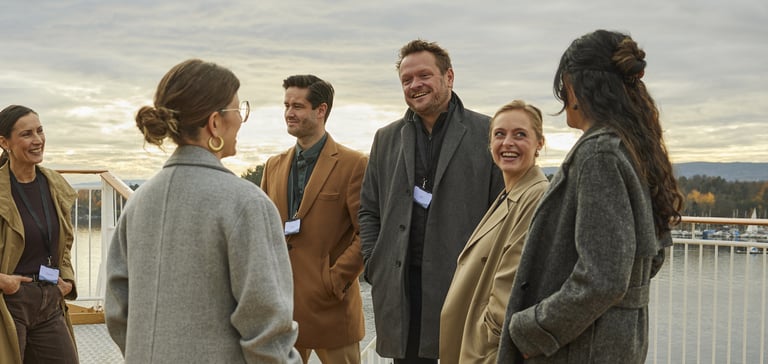 En gruppe mennesker i yttertøy som prater sammen på dekk under en konferanse