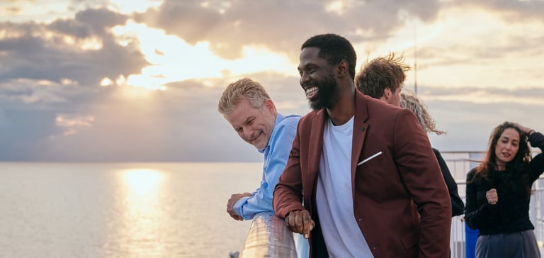 Fire personer som står på et dekk med havet og solnedgang i bakgrunnen.