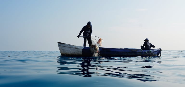 To personer på en liten båt midt på et rolig vann, hvor en håndterer et fiskegarn.