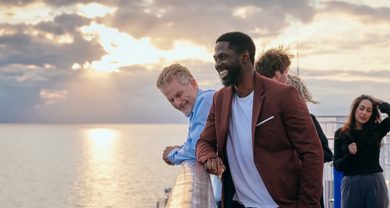 Fire personer som står på et dekk med havet og solnedgang i bakgrunnen.