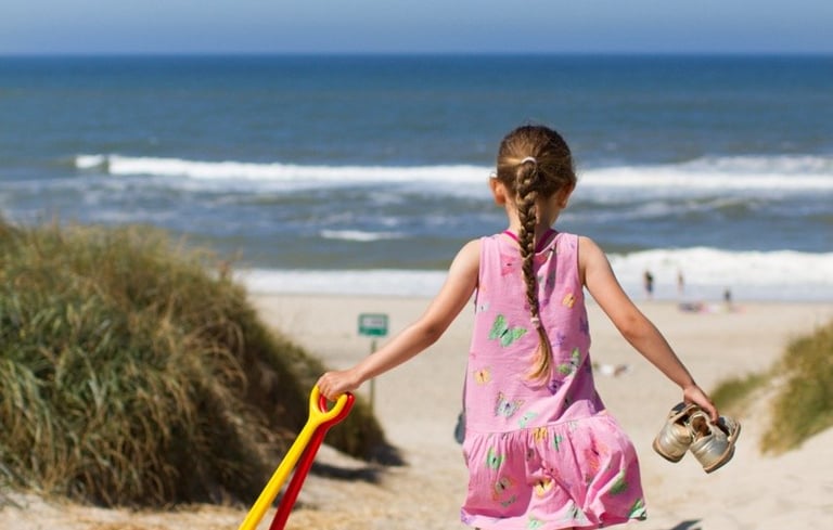 Jente som går ned en sandsti mot stranden.