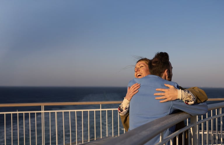 To personer som omfavner hverandre på en balkong med utsikt over havet.