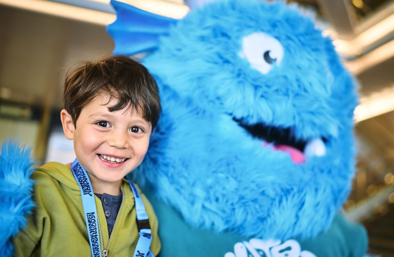 Person som står ved siden av en stor blå lodden maskot med hvite øyne og et stort smil i Matrosklubben.