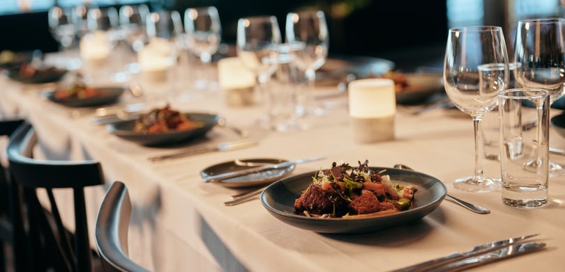 Elegant dekket spisebord med hvit duk, salat, bestikk, stearinlys og vinglass