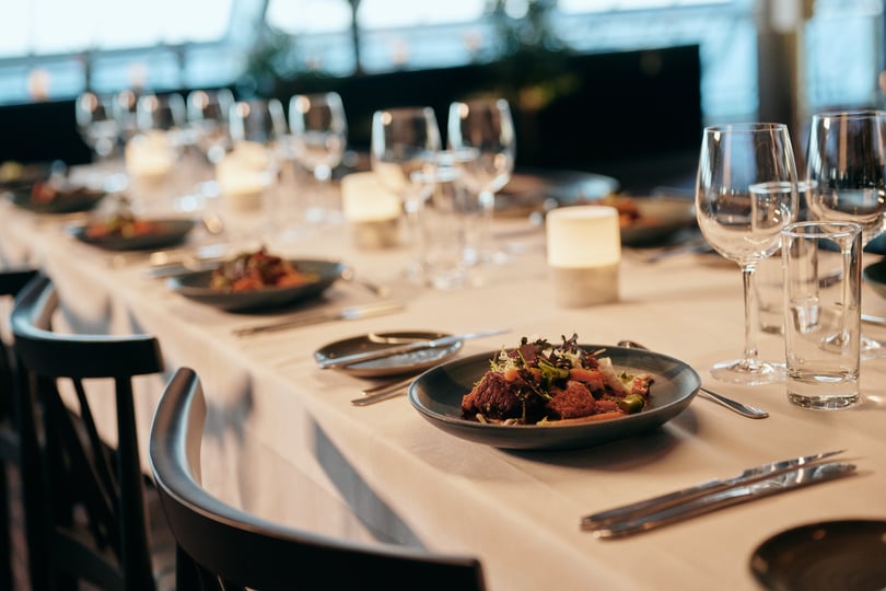 Elegant dekket spisebord med hvit duk, salat, bestikk, stearinlys og vinglass
