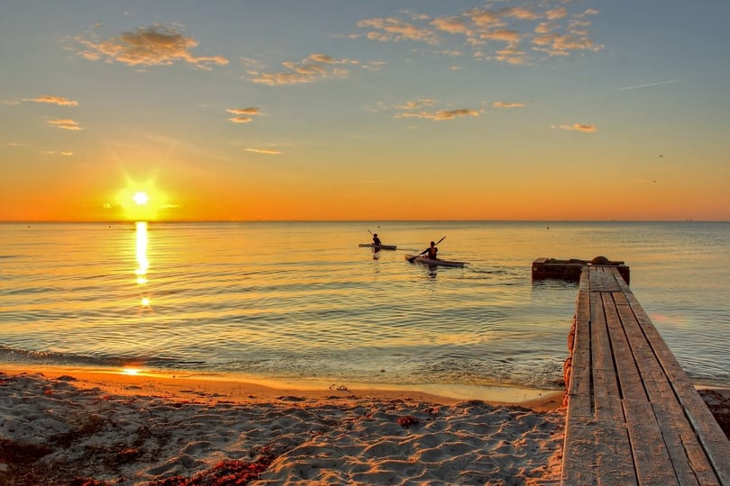 Fredelig strandscene ved solnedgang med to personer som padler kajakk.