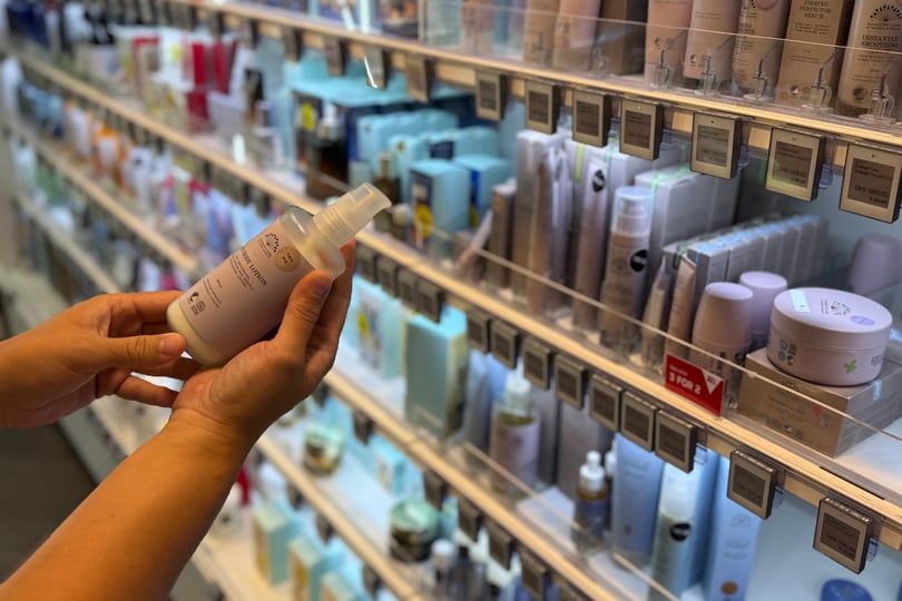 Person holder en hudpleieflaske i en butikkgang med skjønnhetsprodukter